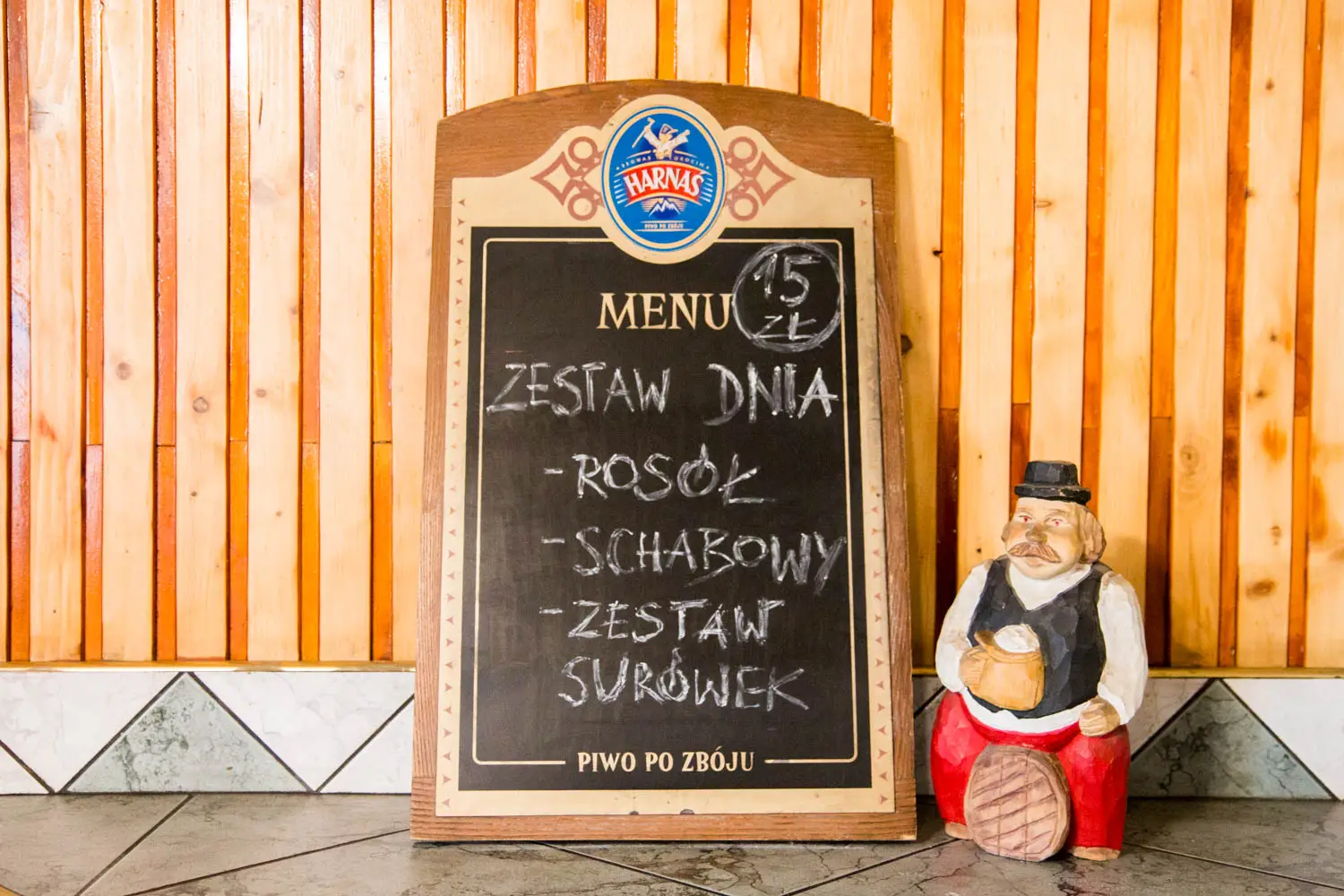 Tablica z zestawem dnia przy ladzie w Barze Janosik, obok drewniana figura górala